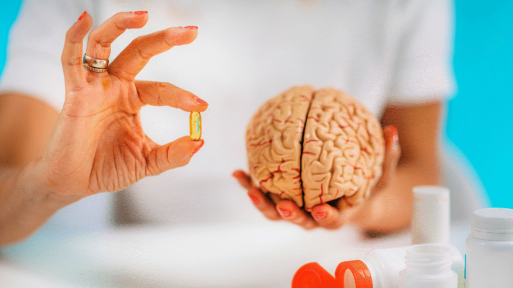osoba trzymająca model mózgu i kapsułkę, biurko z suplementami diety