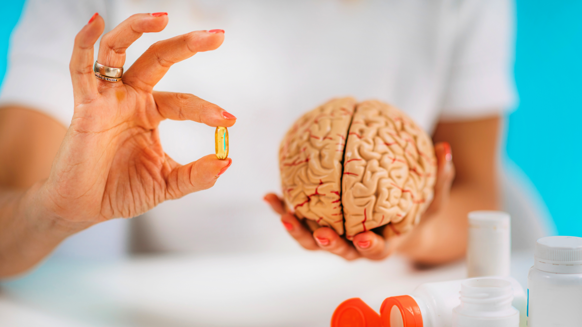 osoba trzymająca model mózgu i kapsułkę, biurko z suplementami diety