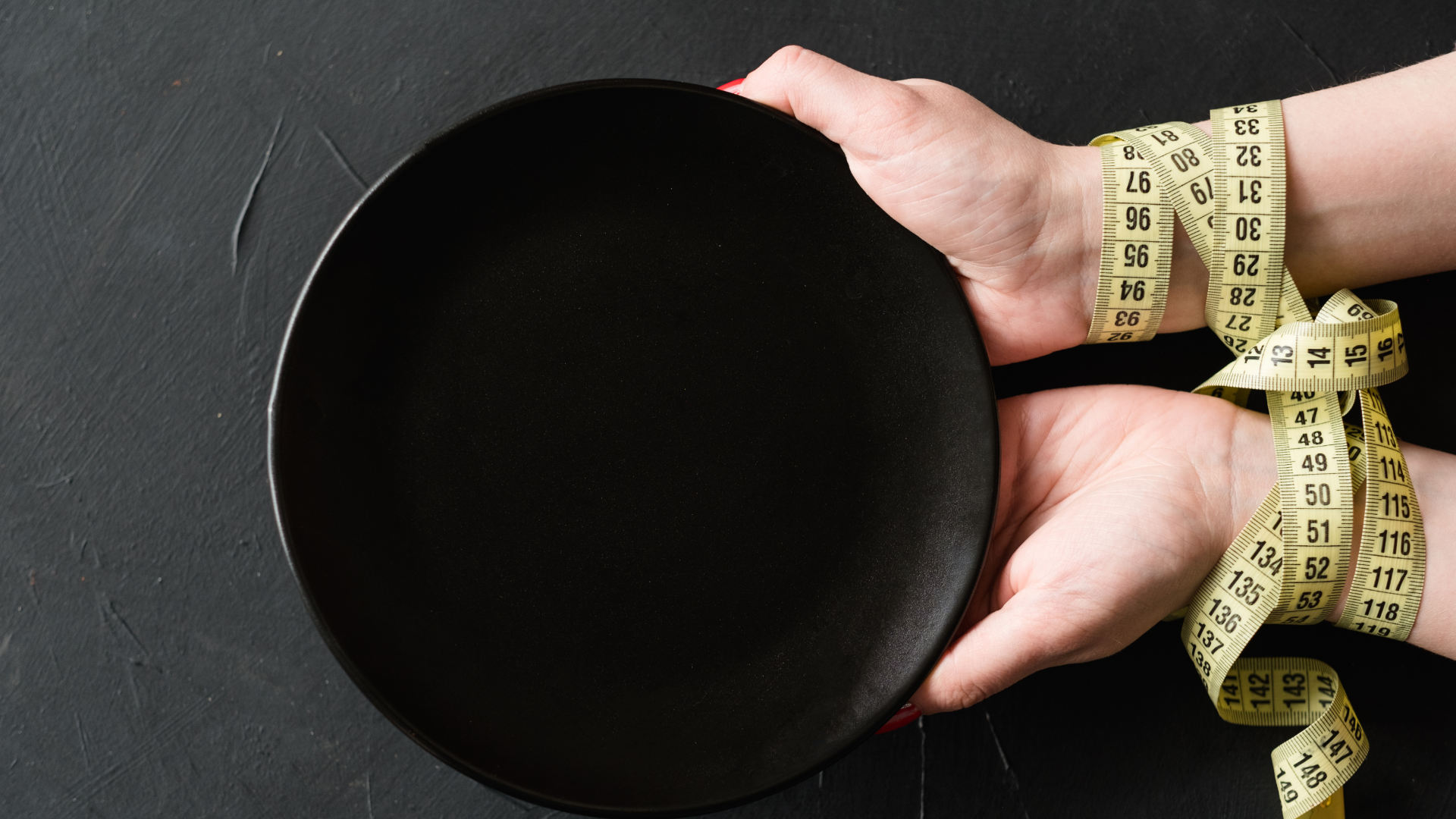 czarny talerz, ręce owinięte miarą krawiecką